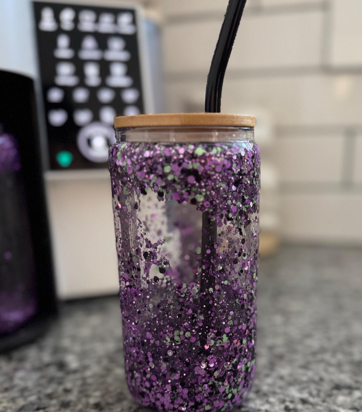 Purple, Mint and Black Glitter 16oz Snow Globe Tumbler with black bent glass straw in front of ice coffee maker