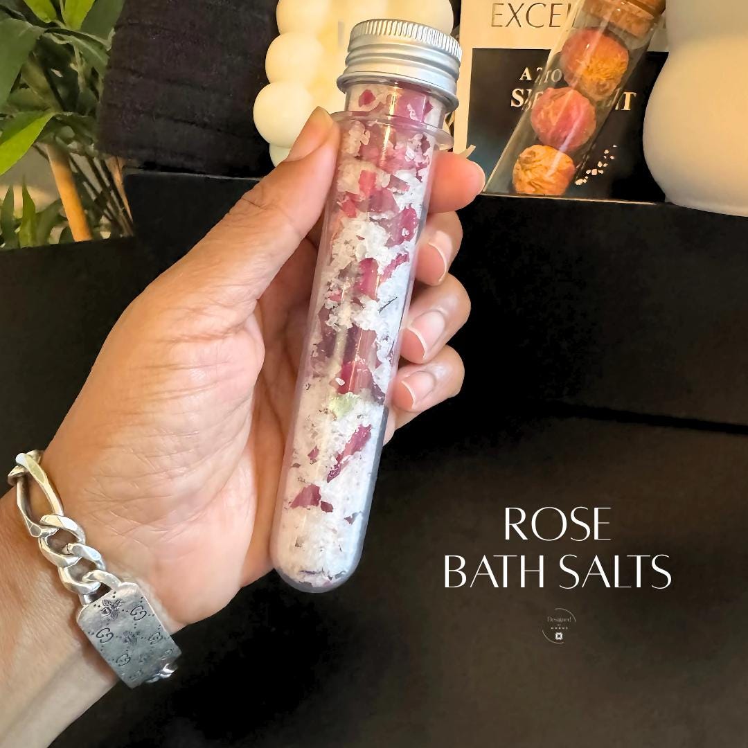 Glass tube filled with rose petal bath salts held in hand, included in spa relaxation gift box.
