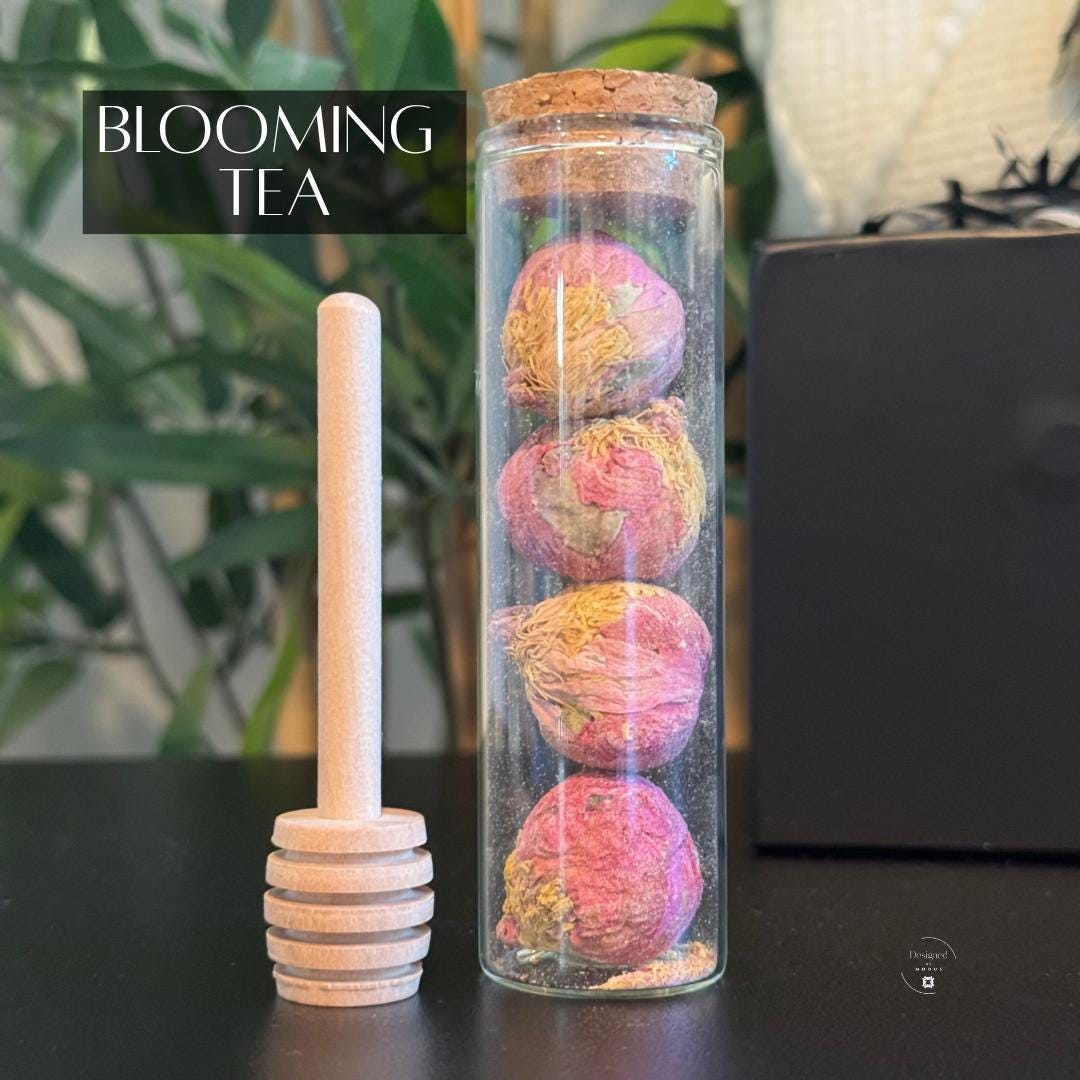 Glass tube with rose blooming tea balls and wooden honey dipper, included in cozy holiday gift box.