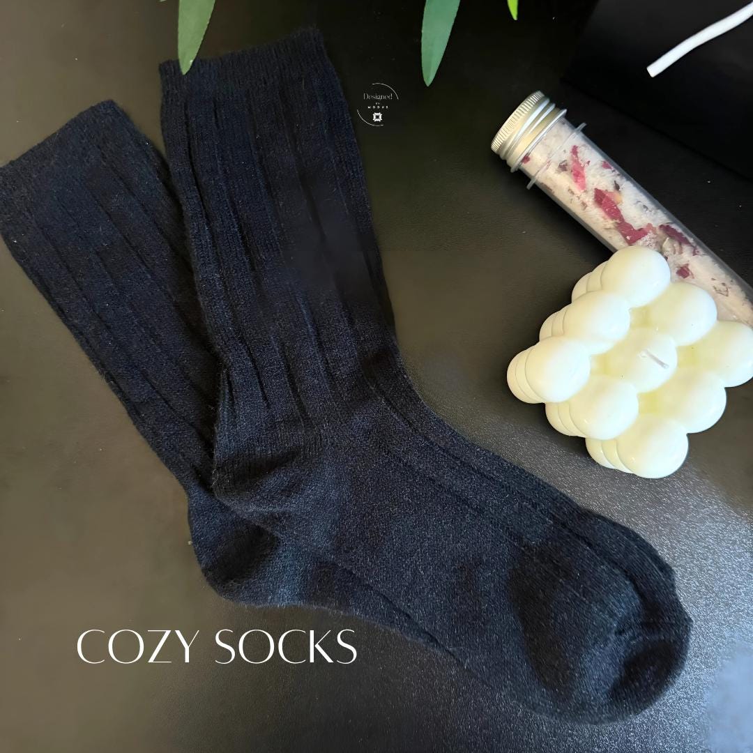 Pair of black ribbed cozy socks next to bubble candle and bath salts, part of winter self-care gift set.