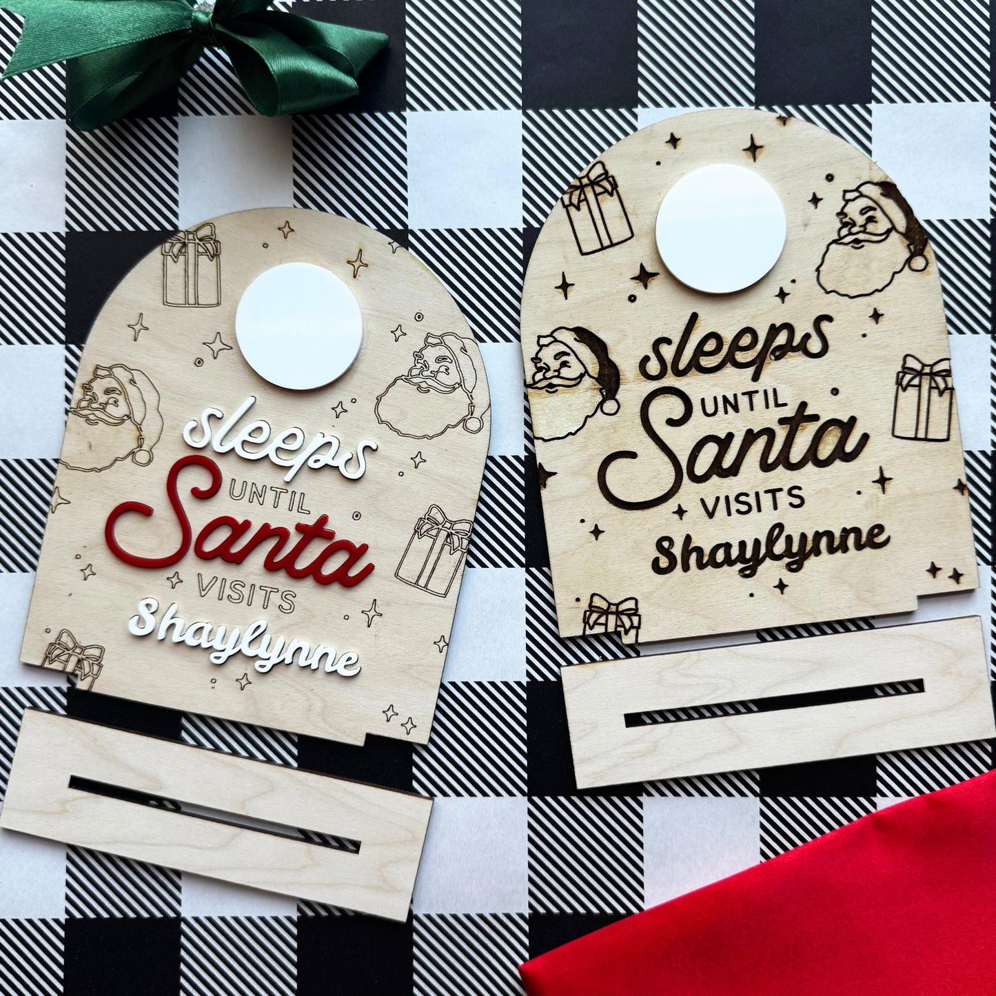 Side-by-side view of two “Sleeps Until Santa” wooden countdown signs, engraved and raised versions, shown with removable base pieces and green ribbon decor.