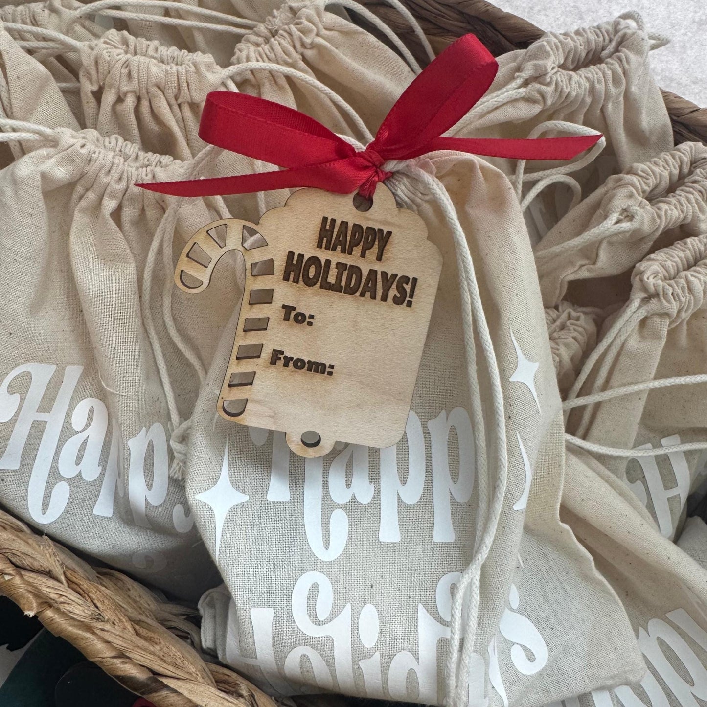 Candy Cane gift tag tied with red ribbon on a linen “Happy Holidays” bag, styled in a woven holiday basket.