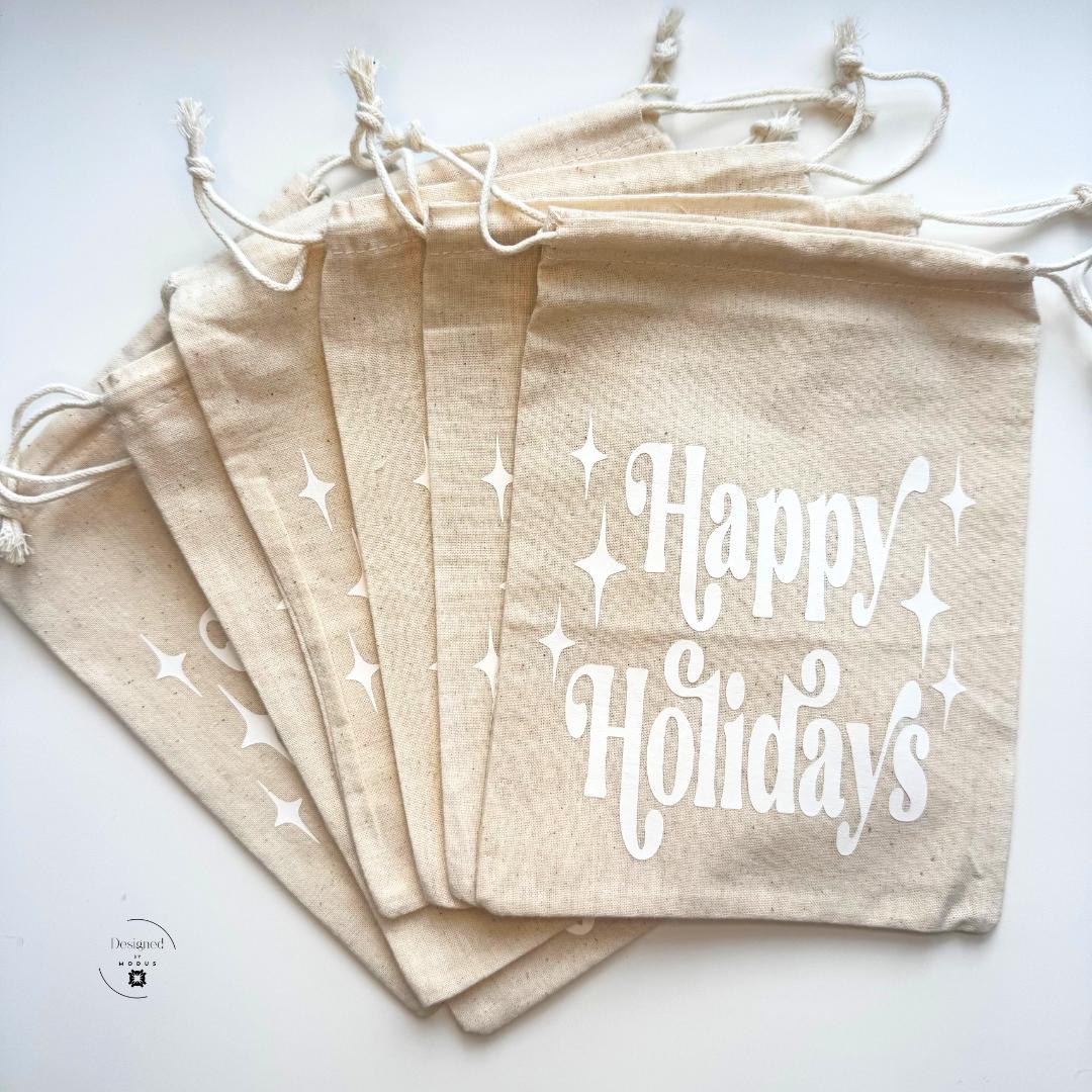 Set of beige drawstring “Happy Holidays” gift bags with white festive lettering, perfect for packaging Christmas slime kits or small stocking stuffers.