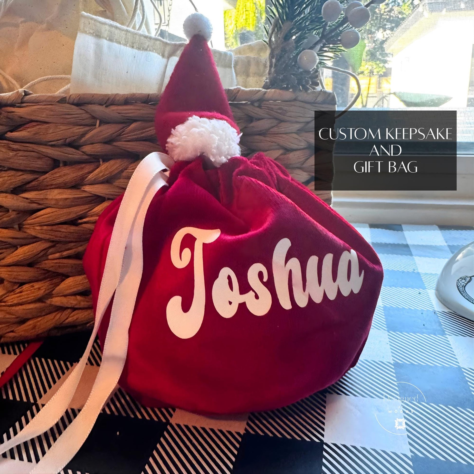 Personalized red velvet Santa hat gift bag with white pom-pom and custom name in bold white lettering.