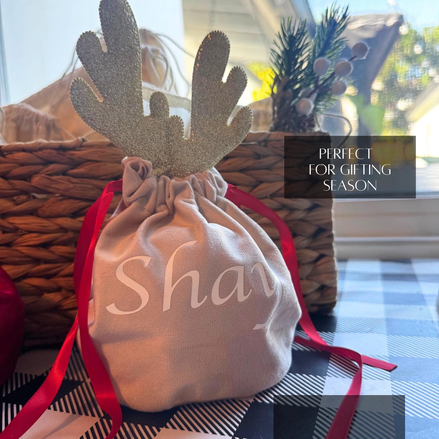 Custom beige velvet gift bag with glitter reindeer antlers and red ribbon, personalized name in white script.
