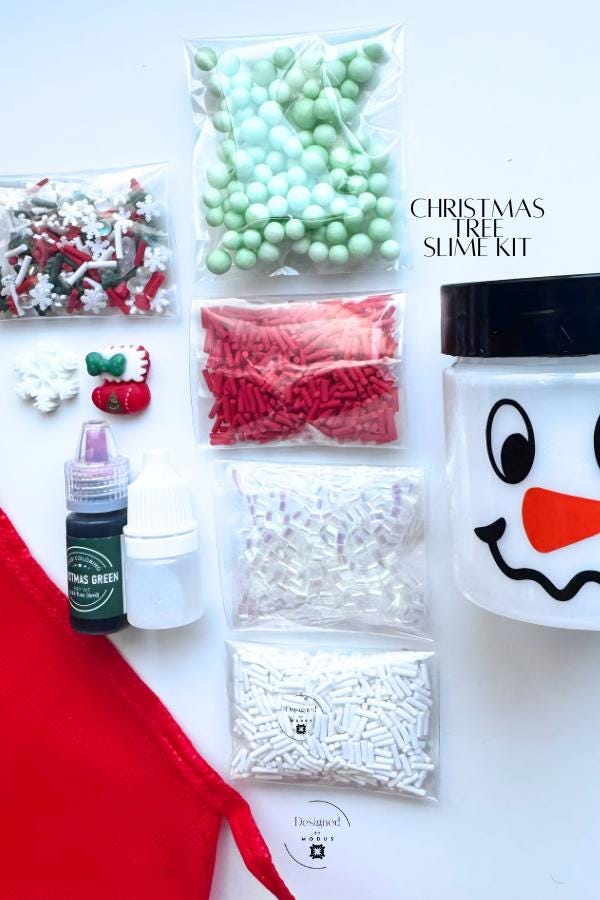 Christmas Tree Slime Kit with red apron, pre-made white slime in snowman jar, green dye, activator bottle, and assorted red, green, and white holiday mix-ins including sprinkles, foam beads, and charms displayed flat lay style.