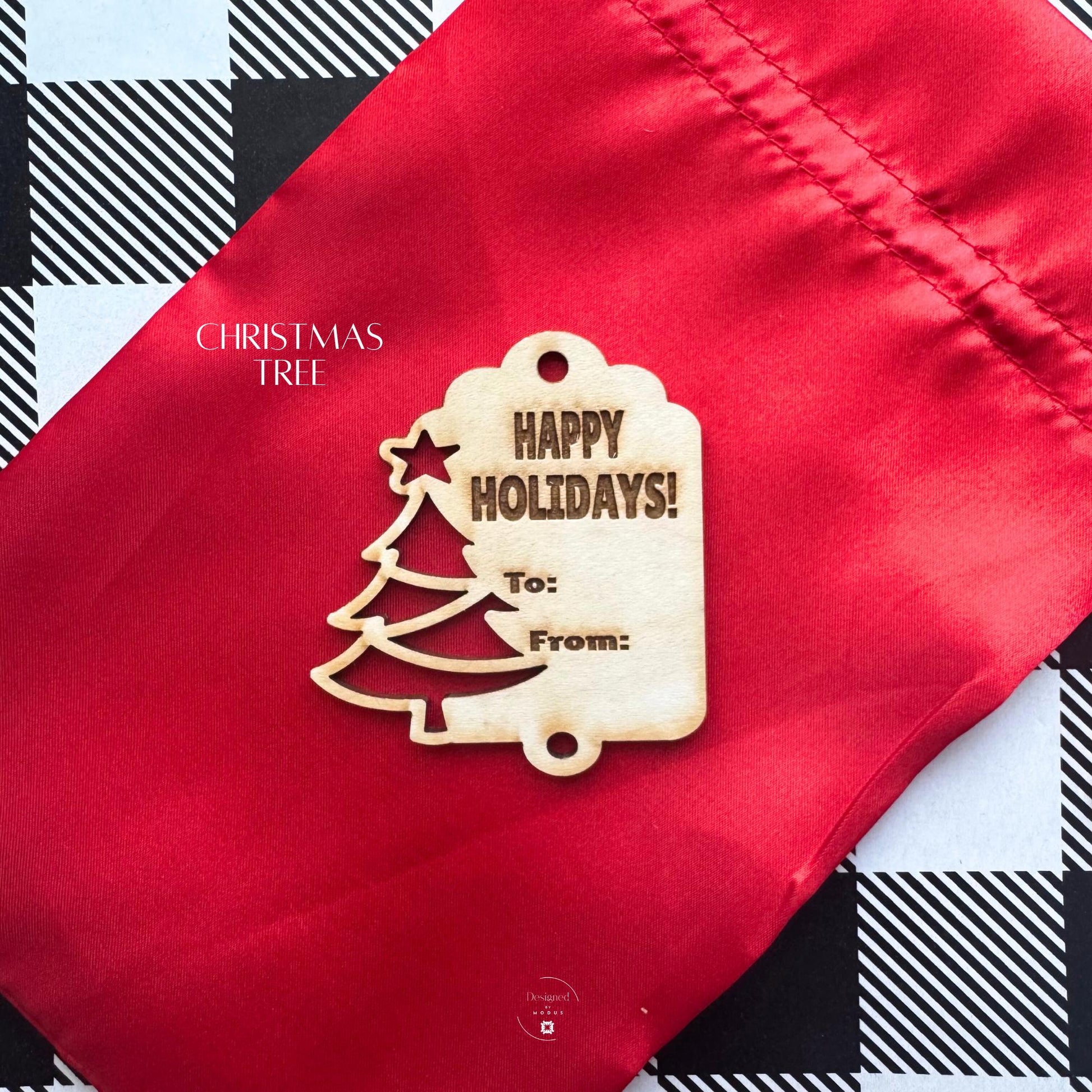 Close-up of Christmas Tree wooden gift tag engraved with “Happy Holidays” and “To/From” text, displayed on red fabric bag.