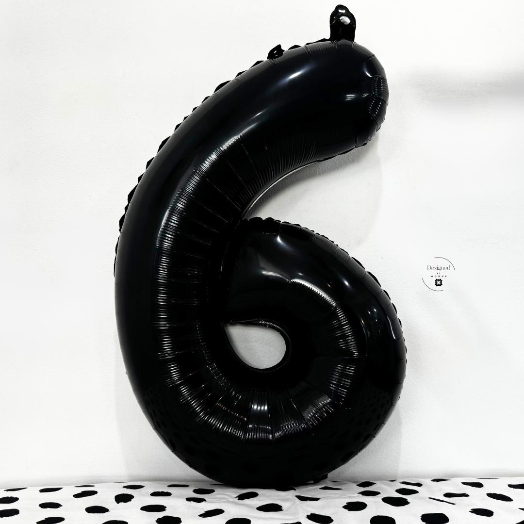 Glossy black number 6 foil balloon on white background with dotted black fabric.