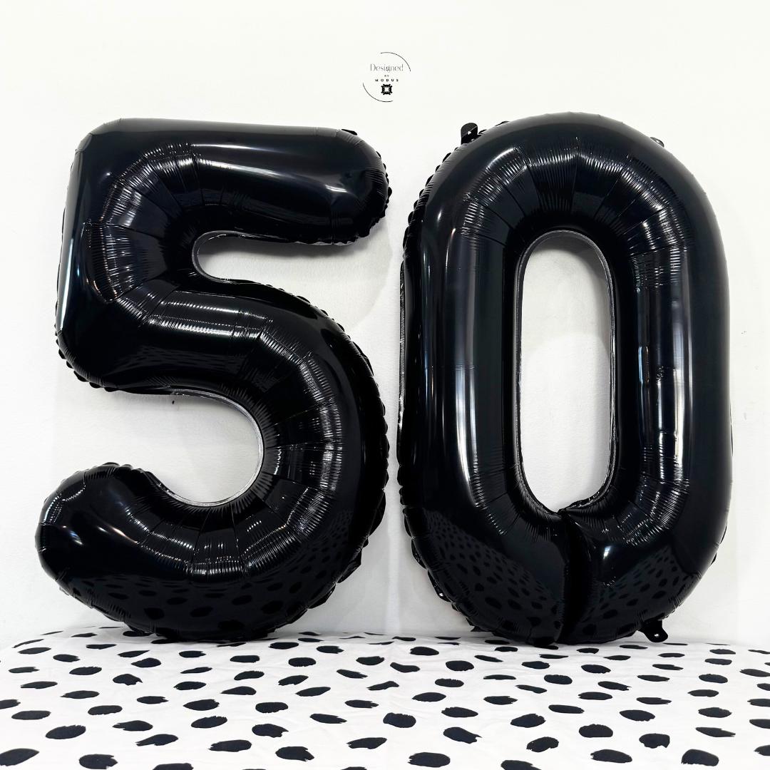 Black number 5 and number 0 foil balloons together on white wall with dotted surface.
