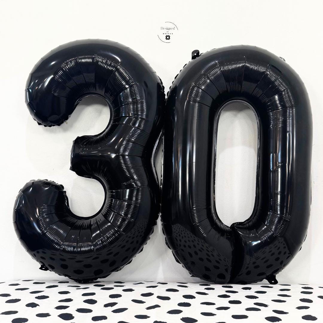 Black number 3 and number 0 foil balloons together on white wall with dotted surface.