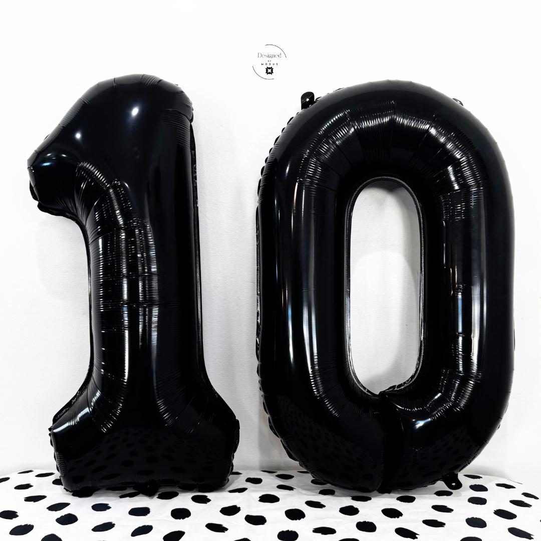 Black number 1 and number 0 foil balloons together on white wall with dotted surface.