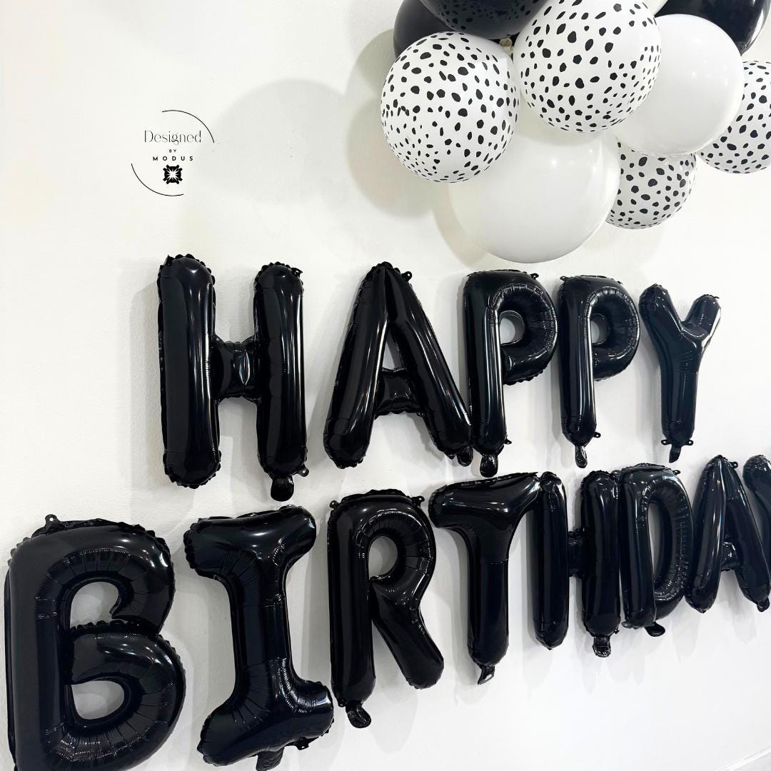 Diagonal view showing depth and shine of black letter balloons against white wall.