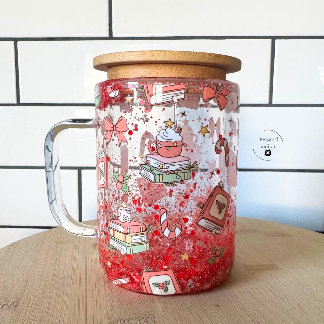 Festive glass tumbler with lid and straw, featuring red glitter snow effect.
