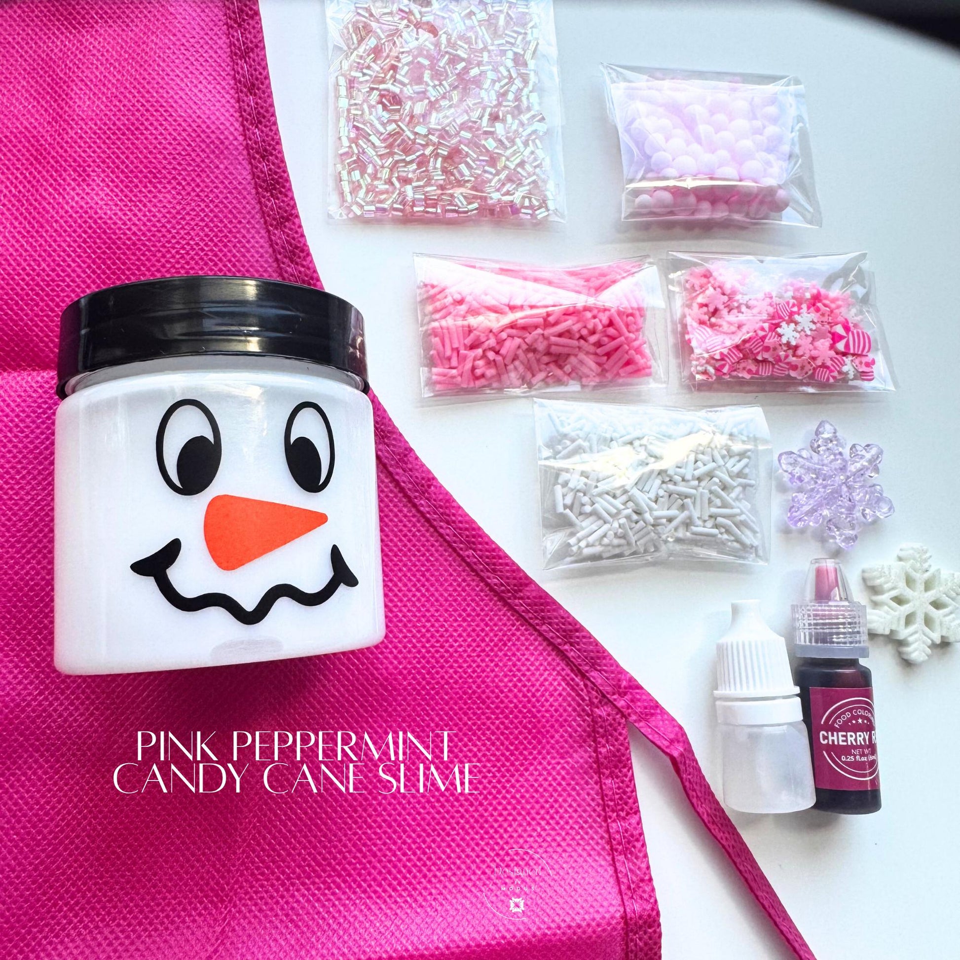 Pink Peppermint Candy Cane Slime Kit with white slime in snowman jar, pink apron, dye, activator, and assorted pink, white, and iridescent mix-ins displayed flat lay.