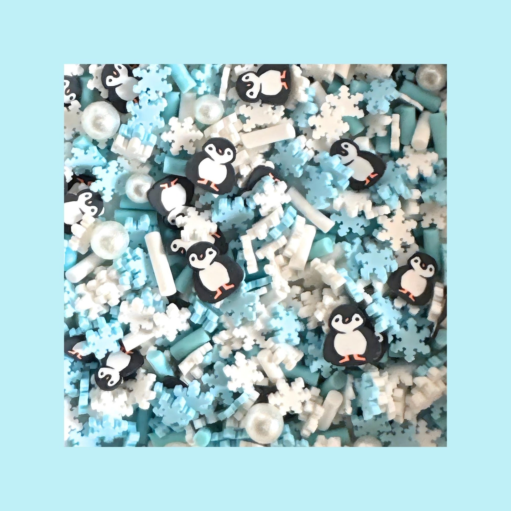 Close-up of penguin and snowflake polymer sprinkles in white, blue, and black tones used for winter slime crafts.