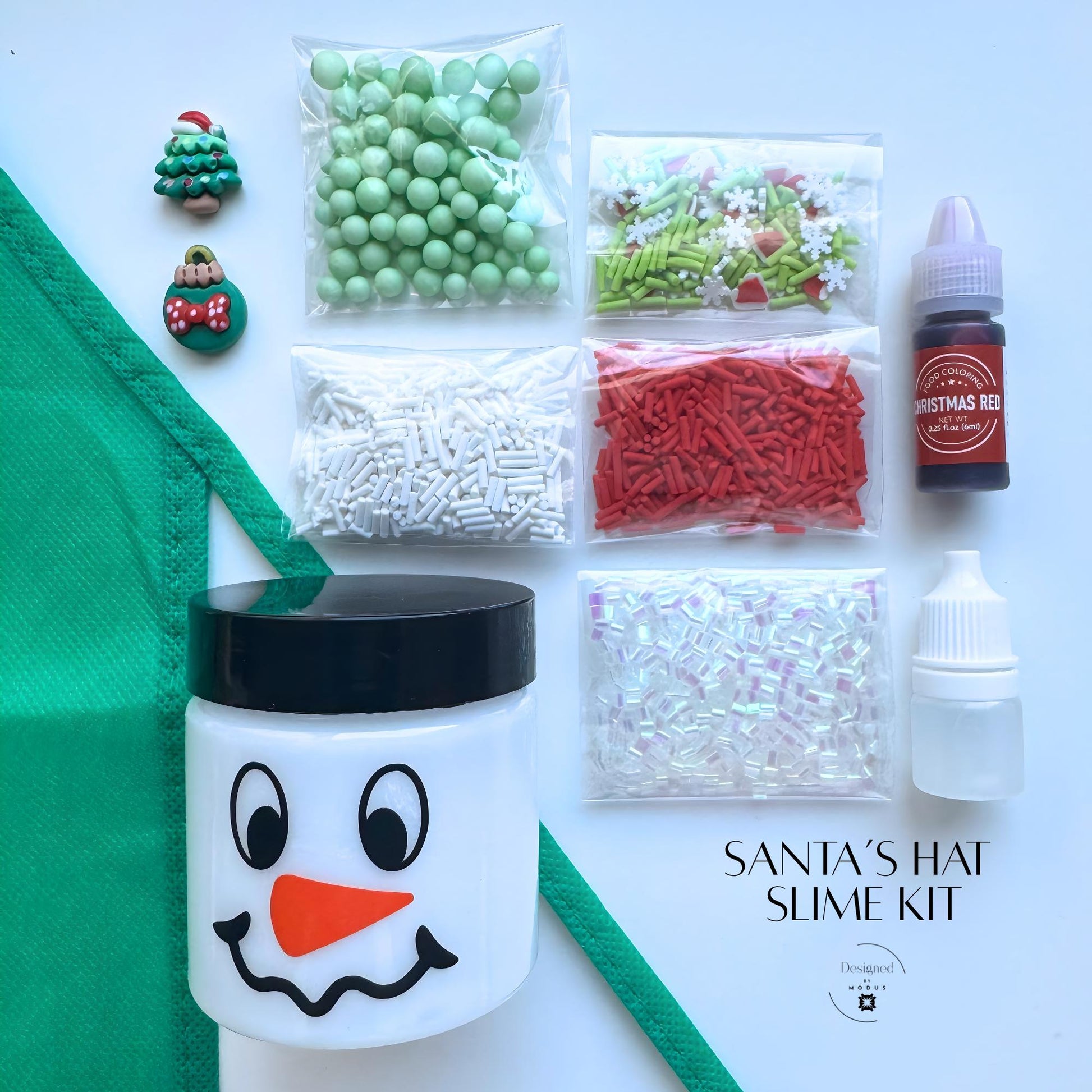 Santa’s Hat Slime Kit flat lay with green apron, snowman jar, and red, green, and white mix-ins labeled “Santa’s Hat Slime Kit.”