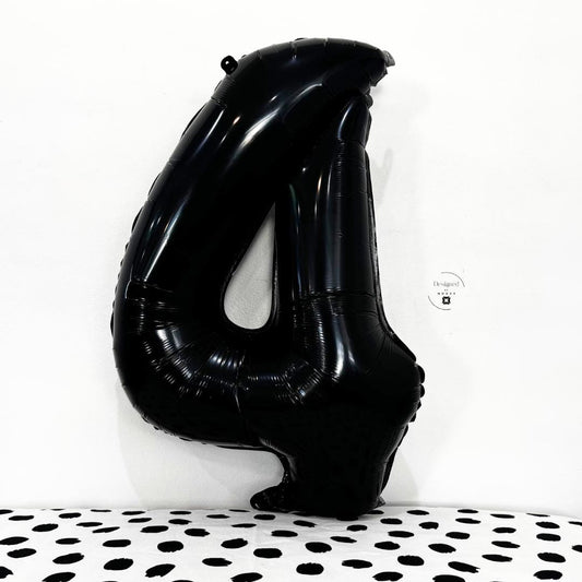 Large black number 4 foil balloon leaning on white wall with black dot pattern fabric.