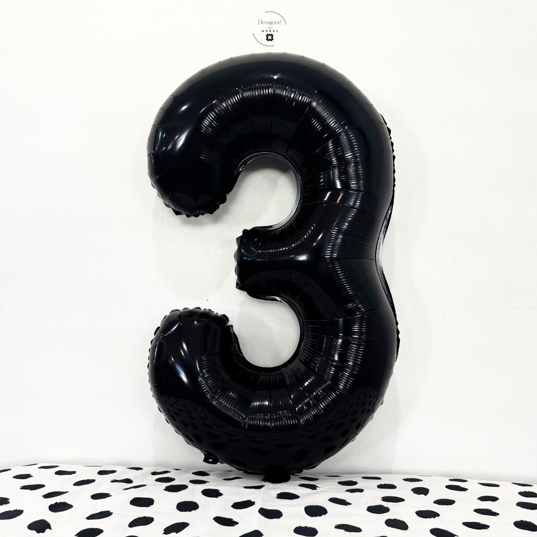 Black number 3 foil balloon on minimalist white background with dotted fabric surface.