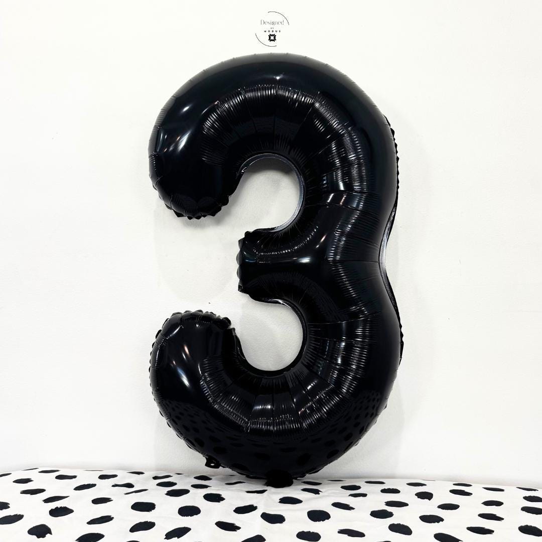 Black number 3 foil balloon on minimalist white background with dotted fabric surface.
