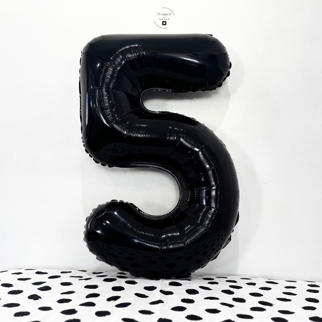 Glossy black number 5 foil balloon on white background with dotted black fabric.