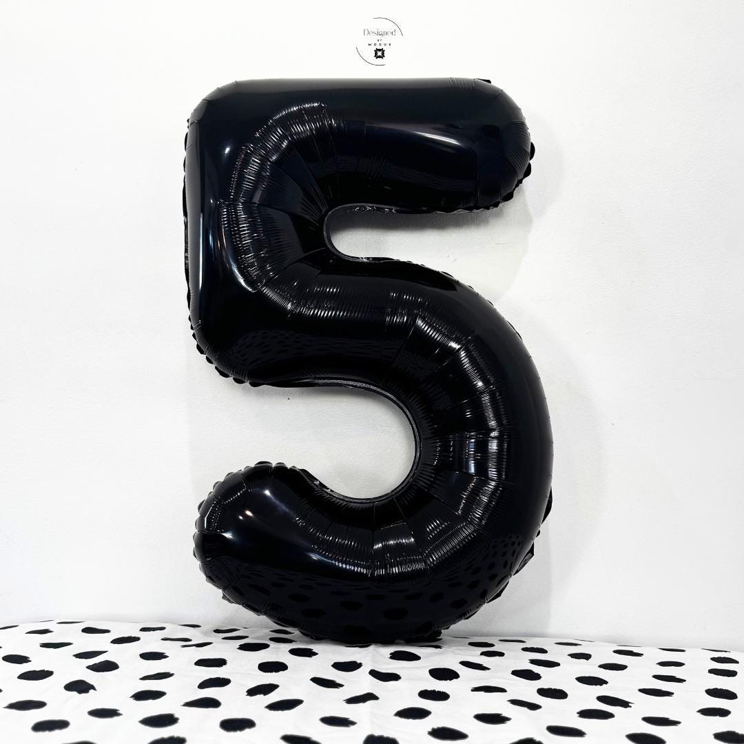 Glossy black number 5 foil balloon on white background with dotted black fabric.