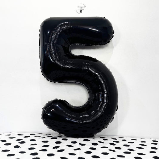Glossy black number 5 foil balloon on white background with dotted black fabric.