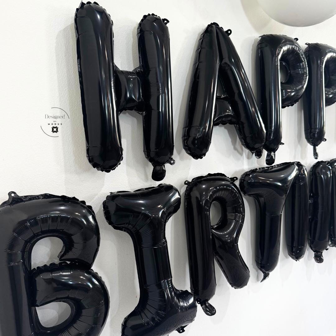 Glossy foil texture of black letter balloons reflecting light on white wall.