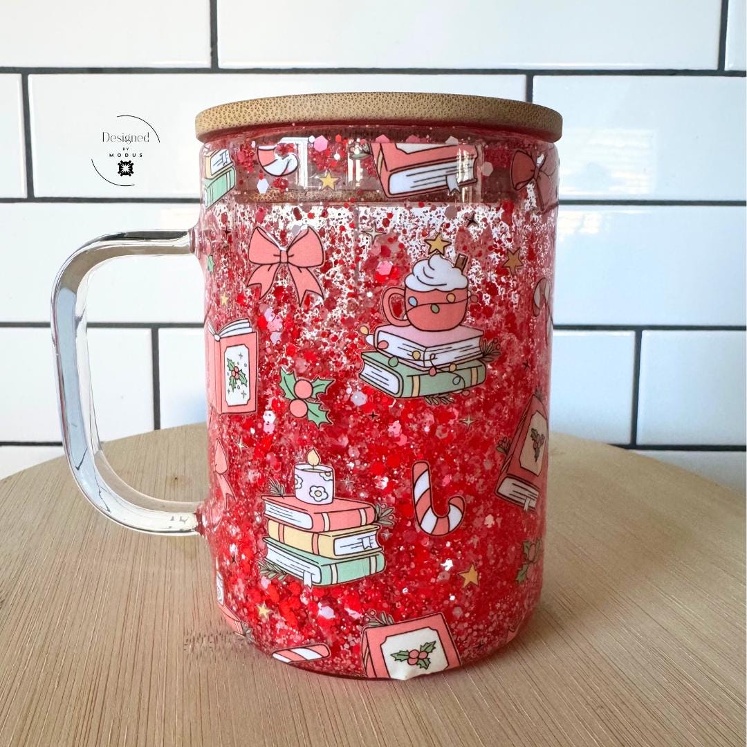 Red glitter glass cup with festive Christmas book and cocoa design, bamboo lid, and clear handle.