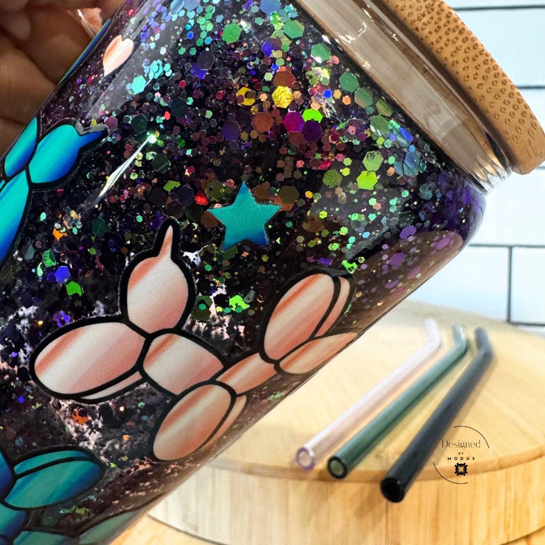 Close-up of colorful glitter details on clear glass mug with teal and pink balloon dogs.