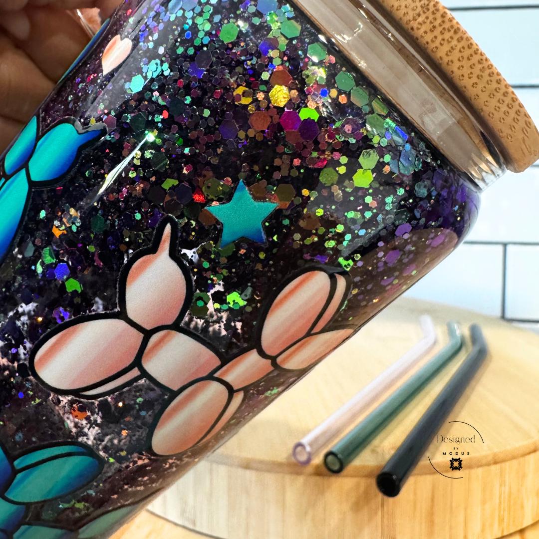 Close-up of colorful glitter details on clear glass mug with teal and pink balloon dogs.