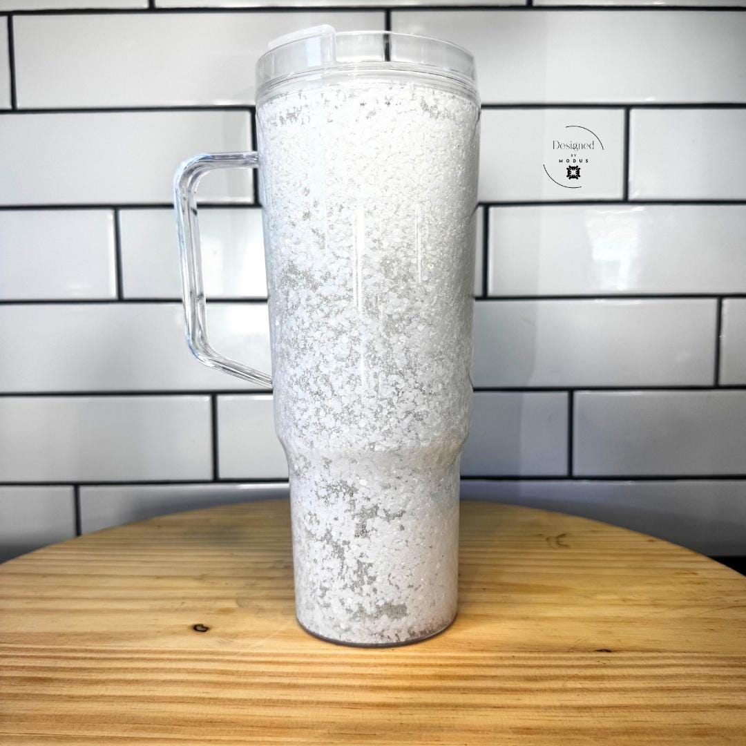 White iridescent glitter snow globe tumbler with clear handle on wooden table