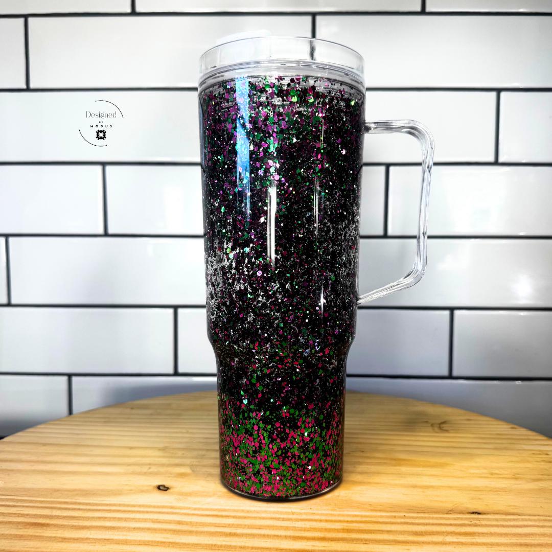 Side view of pink and green glitter snow globe cup with handle against white tile background-Unique Gift Idea Glitter Snow Globe Tumbler Statement Accessory Holographic Cup Design Hot Pink Green Sparkle Effect Floating Glitter Experience Bold Aesthetic Drinkware Clear Handle Feature Slide Lid Convenience 40oz Capacity Perfect