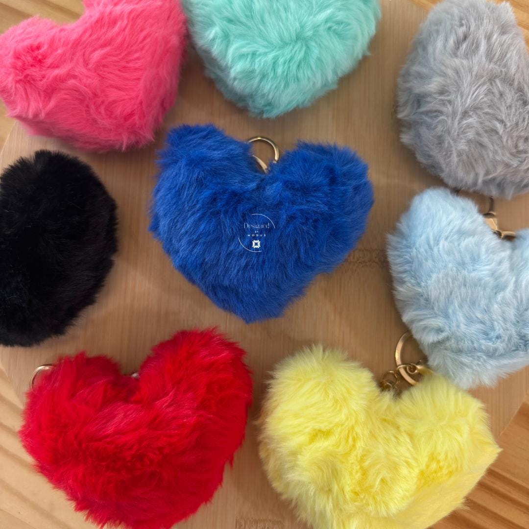 Fuzzy heart keychains in multiple colors displayed on wood surface
