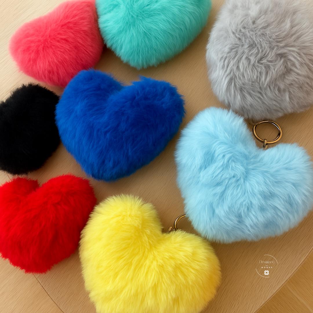 Fuzzy heart keychains in multiple colors displayed on wood surface