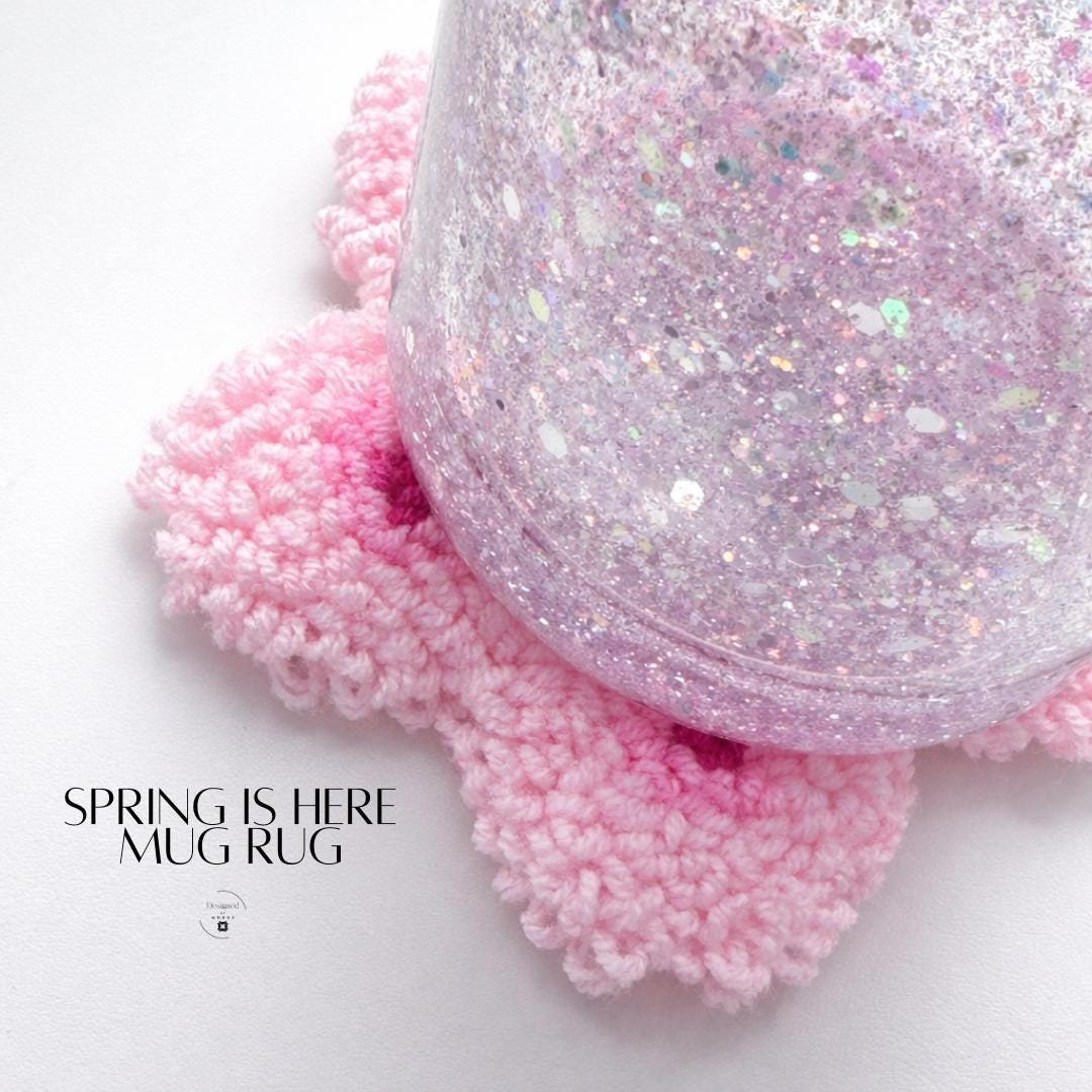 Handmade cherry blossom mug rug shaped like a pink sakura flower with plush tufted texture, featuring soft blush petals, deep magenta accents, and a bright yellow center, displayed on a clean white background as a spring aesthetic coffee coaster and floral desk decor accessory.