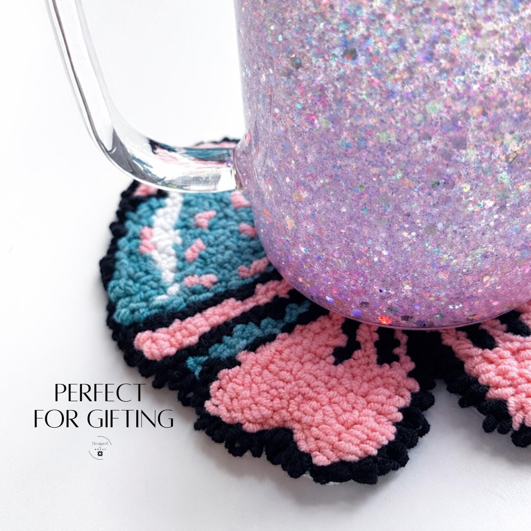 Handmade pink bow mug rug with blue and black tufted detailing, coquette style bow shaped coffee coaster and tea cup mat, cute girly aesthetic desk decor and coffee bar accessory displayed on white background.