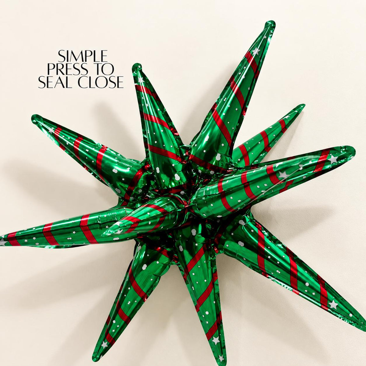 Green and red Christmas starburst Mylar balloon with dimensional pointed arms, metallic foil finish, red diagonal stripes and white stars. Festive balloon accent for DIY Christmas balloon garlands, holiday party arches, Christmas photo booths, winter wonderland displays, traditional Christmas party decorations, classroom celebrations, office holiday parties and seasonal balloon arrangements.