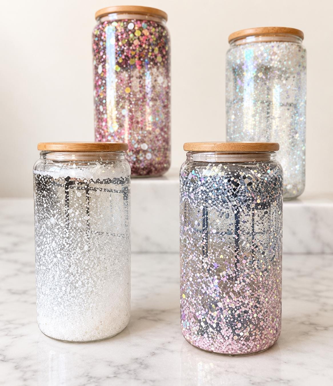 Four glass snow globe tumblers featuring sparkling glitter suspended in water between double glass walls, natural bamboo lids and glass drinking straws. White, silver iridescent and colorful multicolor glitter finishes create a floating snow globe effect. Reusable glass cups for iced coffee, cold brew and cold beverages. Christmas gift for women, coffee lover gift, holiday drinkware, teacher Christmas present, coworker gift and Secret Santa gift idea.